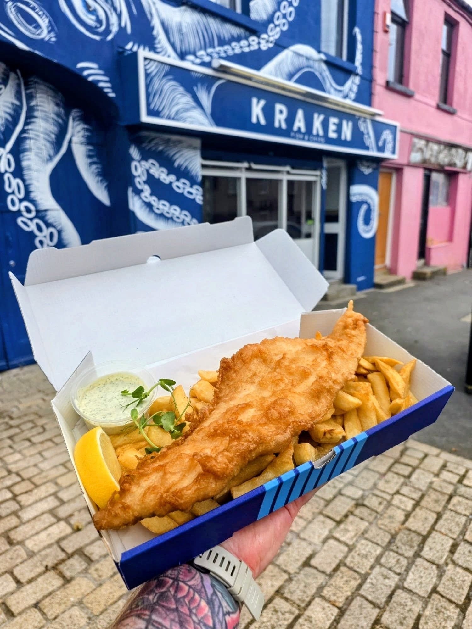 A freshly cooked fish supper in a Kraken box, held outside the shop